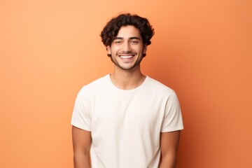 Portrait of a grinning man in his 20s wearing a simple cotton shirt against a pastel orange background. AI Generation