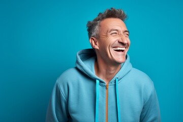 Obraz premium Portrait of a joyful man in his 50s wearing a zip-up fleece hoodie against a soft blue background. AI Generation