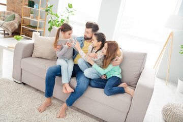 Obraz premium Portrait of four persons sit on sofa handsome guy cuddle girls point finger funny sister spend weekend home indoors