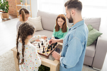 Portrait of attractive focused idyllic family playing chess with daddy spending holiday at home house living-room indoors