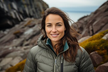 Portrait of a happy woman in her 30s donning a durable down jacket against a rocky cliff...