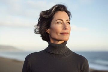 Portrait of a tender woman in her 50s wearing a classic turtleneck sweater against a serene seaside background. AI Generation