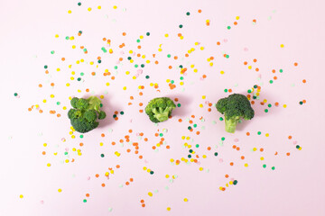 Broccol with colorful paper confetti on pink background. Flat lay.