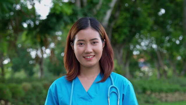 Portrait of confident, happy, and smiling Asian medical woman doctor or nurse wearing blue scrubs uniform, Outdoor