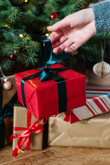 An unrecognizable female hand puts a gift under the Christmas tree.