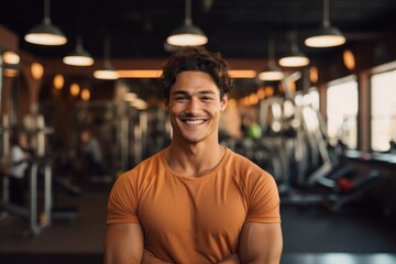 Portrait of a grinning man in his 20s donning a trendy cropped top against a dynamic fitness gym...