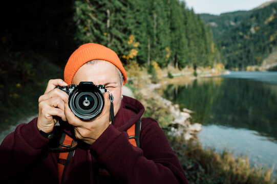 A photographer with a camera in his hands, wearing an orange hat, takes pictures in nature.