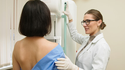 A female doctor in a modern clinic explains the mammography procedure to a topless adult patient...