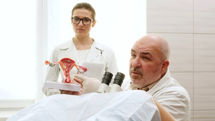 A gynecologist with a laboratory assistant or nurse shows female diseases to a patient using a model of the uterus and ovaries in a gynecological office. Pregnancy, antenatal clinic, women's health.