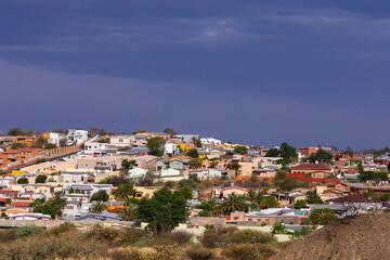 Fototapeta na wymiar The outskirts of Windhoek, Namibia, seen from the highway under a ray of sunshine, with dark cloudy sky in the background
