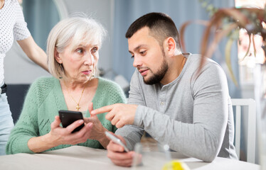 Adult son help an elderly mother learn how to use a smartphone