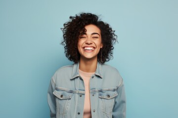 Portrait of a grinning woman in her 30s sporting a rugged denim jacket against a pastel or soft...