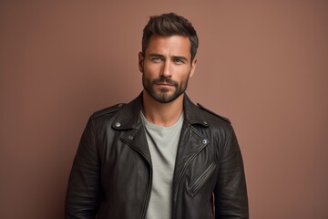 Obraz premium Portrait of a satisfied man in his 30s sporting a classic leather jacket against a pastel or soft colors background. AI Generation
