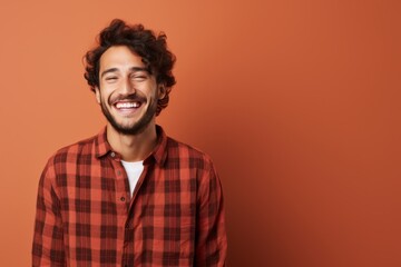Obraz premium Portrait of a happy man in his 20s dressed in a relaxed flannel shirt against a solid color backdrop. AI Generation