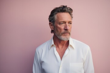 Portrait of a tender man in his 50s wearing a classic white shirt against a solid pastel color...