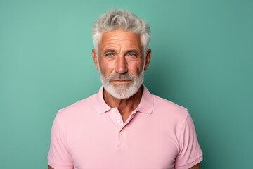 Portrait of a glad man in his 70s wearing a breathable golf polo against a solid pastel color wall....