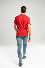 Man in jeans and red t-shirt is walking. Rear view. Full length studio shot isolated on white