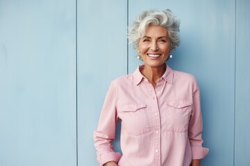 Portrait of a happy woman in her 80s sporting a versatile denim shirt against a solid pastel color...