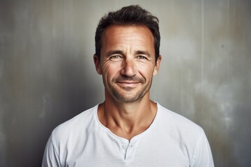 Portrait of a smiling man in his 40s wearing a simple cotton shirt against a bare concrete or plaster wall. AI Generation