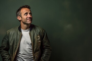 Portrait of a blissful man in his 40s sporting a stylish varsity jacket against a bare concrete or plaster wall. AI Generation