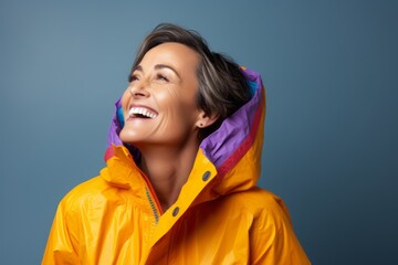 Portrait of a blissful woman in her 50s wearing a vibrant raincoat against a blank studio backdrop....