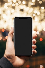 Male hand holding smartphone with blank screen on bokeh lights background.