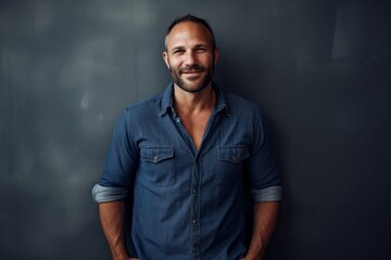 Naklejka premium Portrait of a grinning man in his 40s sporting a versatile denim shirt against a bare monochromatic room. AI Generation