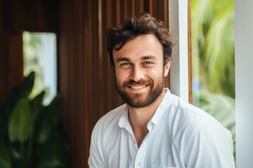 Portrait of a grinning man in his 30s wearing a simple cotton shirt against a stylized simple home office background. AI Generation