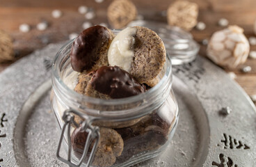 Homemade christmas cookies with poppy seeds and glazed chocolate in a glass jar on a silver plate