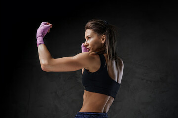 Muscular woman boxer demonstrating striking skills, dressed in sports attire, against a moody dark...
