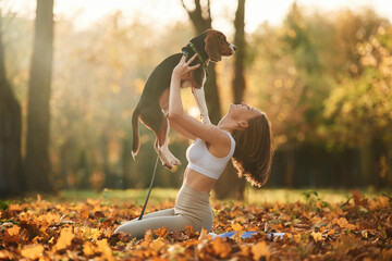 Holding animal in hands. Woman is with her cute dog in the autumn forest