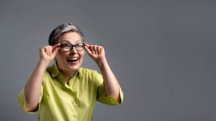surprised 50s elderly woman looking through glasses on green friday sales on grey background