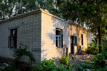 An abandoned brick building with broken windows and overgrown vegetation.