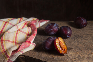 Whole and half of purple plums on wooden background. .