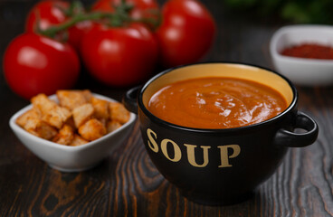 Tomato soup in a black bowl with the inscription Soup on a brown background.