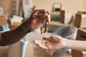 Hand of young African American male real estate agent passing key to new owner of apartment against...