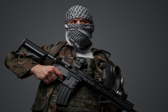 Middle Eastern radical fanatic soldier donning a white keffiyeh and camouflaged field uniform, armed with an automatic rifle, against a gray background