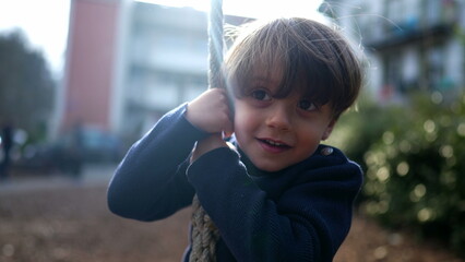 Joyful Child Firmly Gripping and Descending Wire Rope Slide at Public Park in Autumn Fall. Small Boy Gleefully Sliding Down Wire Rope Between Trees in Park