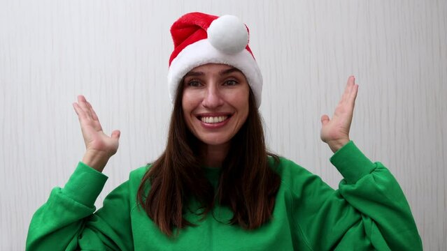 millennial woman in santa claus hat and green hoodie against wall or backdrop with smartphone chroma key screen in hand,deer red horns or fir christmas tree headband.smiling girl having fun