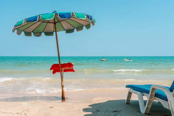 Small cafe menu table under a beach umbrella stands in front of seashore line, sun beach lounge chair, two jetski in a sea