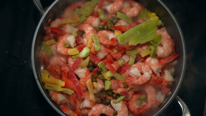 Preparing seafood meal inside pan. Cooking shrimps with vegetables ingredients. Food preparation from top view perspective
