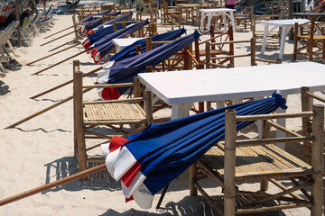 Many closed sun umbrellas on restaurant chairs prepared to be open up, morning time in beach...