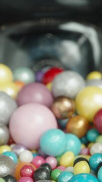 Vertical video. Jar with Sugar Balls in Multicolored Glaze. View from Inside, Balls Scattered on the Table against a Black Background. Dolly slider extreme close-up.