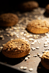 Craft and rustic four oatmeal cookies. Dark food aesthetics, black background with several oat flakes.