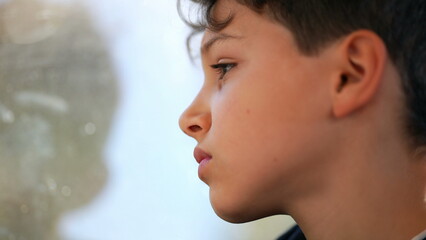Thoughtful young boy gazing at train window looking at landscape pass by while traveling, profile...