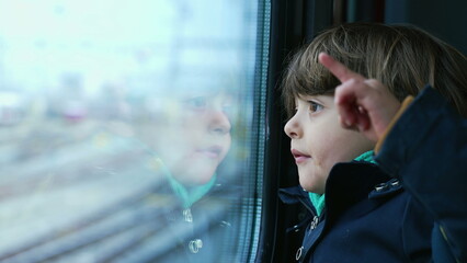 Small boy passenger staring at landscape passing by from trian window. Kid wearing scarf and jacket during autumn fall season travel