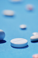 Obraz na płótnie Canvas Medicine and drug concept. Close up shot of white pill on blue background with different tablets on it out of focus.