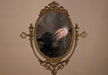 Vintage mirror shows the reflection of the camera and the hands of the photographer capturing photo.