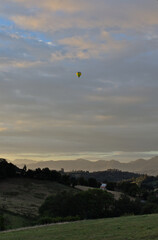 Balloon flying over a green field with trees, cloudy sky during the sunset