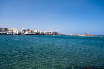 View of the city of Arrecife from the Fermina islet. Turquoise blue water. Sky with big white clouds. Seascape. Lanzarote, Canary Islands, Spain.